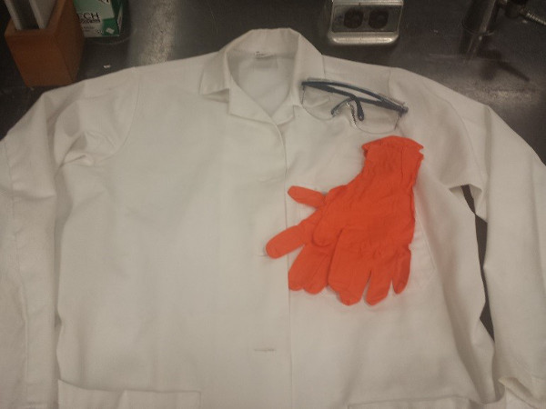 Lab safety equipment including lab coat, goggles, and gloves on a bench for protection in experiments.