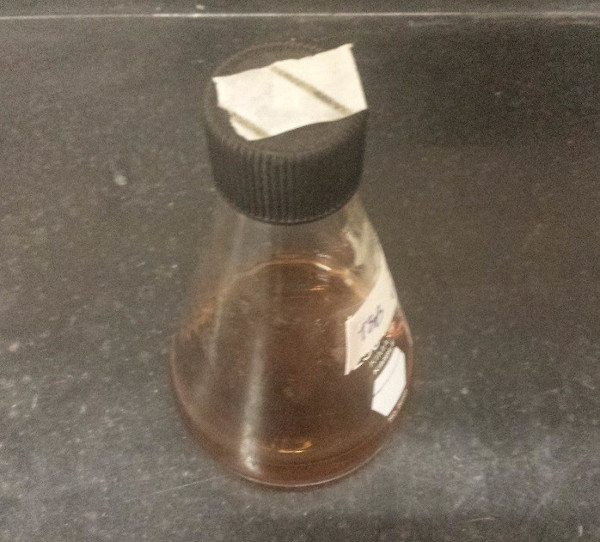 Erlenmeyer flask with brown chemical solution for lab synthesis experiment on dark surface.