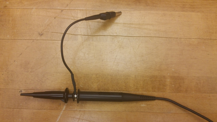 Oscilloscope probe setup on wooden table, used for measuring electrical signals in circuits.