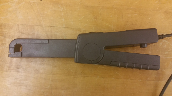 Current clamp sensor for measuring AC/DC current in electrical circuits, shown on wooden surface.