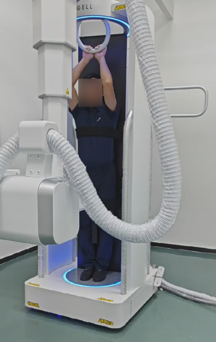 Vertical CT scanner setup for whole-body imaging; person stands inside machine for scanning procedure.