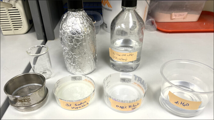 Laboratory setup for chromatography with glassware and reagents. Key solutions labeled for analysis.